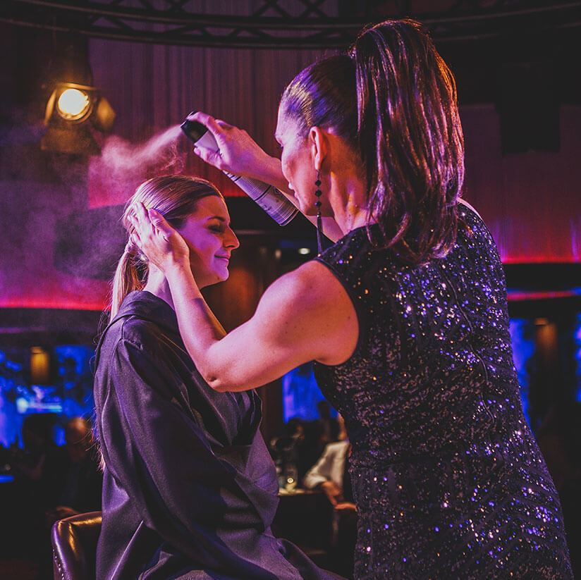 Stylistin frisiert Frau mit Haarspray an der Fashion Night
